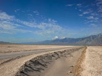 an empty road leads through a barren plain with mountains in the distance above a valley