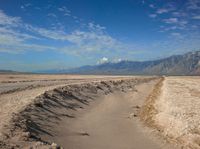 an empty road leads through a barren plain with mountains in the distance above a valley