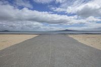 the empty road winds away from the beach near the water's edge and clouds over the mountains