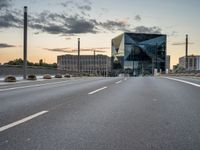 an empty road runs past a building with a glass window in the center and buildings behind it