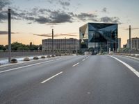 an empty road runs past a building with a glass window in the center and buildings behind it