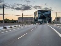 an empty road runs past a building with a glass window in the center and buildings behind it