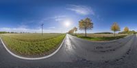 an empty road is next to a large field with trees and a blue sky behind it