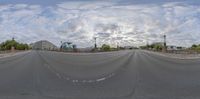 a wide view of the empty road in a city with street lights and a cloudy sky