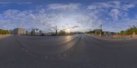 an empty road with a big city in the background during sunset on a partly cloudy day