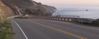 the ocean and mountains are empty on a road with a bike on it and on a bike rack