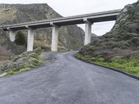 an empty road near some mountains with a bridge over it on both sides of the mountain