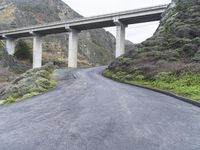 an empty road near some mountains with a bridge over it on both sides of the mountain