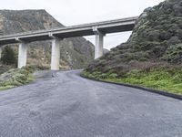 an empty road near some mountains with a bridge over it on both sides of the mountain