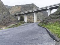 an empty road near some mountains with a bridge over it on both sides of the mountain