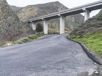 an empty road near some mountains with a bridge over it on both sides of the mountain