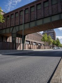 an empty road surrounded by brick buildings and an overpassing bridge over the street