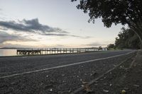 an empty road on the side of the road near a bridge and ocean water at sunset