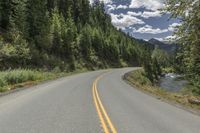 an empty road passes by some mountains and trees in the background with a river under it