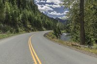 an empty road passes by some mountains and trees in the background with a river under it