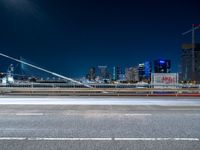 a picture of an empty road, which is next to a building at night with city lights