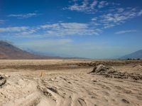 a sign on a post marks an empty road near a desert landscape with a mountain and cloud covered sky