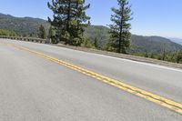 the empty road is along the hillside top with a view of the ocean and trees