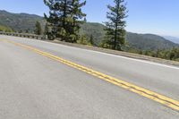 the empty road is along the hillside top with a view of the ocean and trees