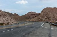 the empty road has several yellow markings along it and the mountains surrounding it with red rocks