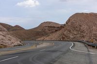 the empty road has several yellow markings along it and the mountains surrounding it with red rocks