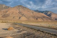 an empty road passing through the mountains in the desert, with a lone bench and horse in the distance