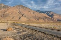 an empty road passing through the mountains in the desert, with a lone bench and horse in the distance