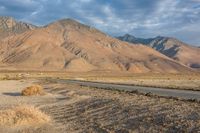 an empty road passing through the mountains in the desert, with a lone bench and horse in the distance