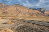 an empty road passing through the mountains in the desert, with a lone bench and horse in the distance