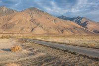 an empty road passing through the mountains in the desert, with a lone bench and horse in the distance