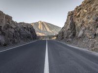 the long and straight empty road passes through a canyon and mountains in the morning sun