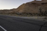 a empty road with a mountain in the distance and a car parked on the side