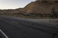 a empty road with a mountain in the distance and a car parked on the side