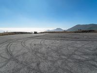 an empty road with cars driving down it and mountains in the background and blue sky above