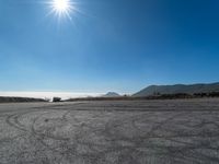 an empty road with cars driving down it and mountains in the background and blue sky above