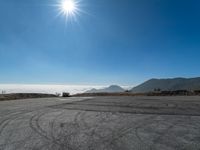 an empty road with cars driving down it and mountains in the background and blue sky above