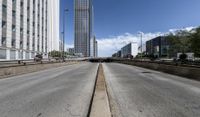 an empty road between two high rise buildings with the top of a freeway crossing to its side