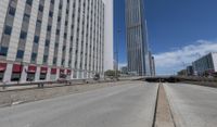 an empty road between two high rise buildings with the top of a freeway crossing to its side