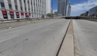 an empty road between two high rise buildings with the top of a freeway crossing to its side