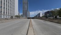 an empty road between two high rise buildings with the top of a freeway crossing to its side