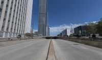 an empty road between two high rise buildings with the top of a freeway crossing to its side