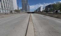 an empty road between two high rise buildings with the top of a freeway crossing to its side