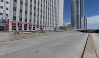 an empty road between two high rise buildings with the top of a freeway crossing to its side