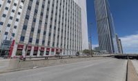 an empty road between two high rise buildings with the top of a freeway crossing to its side