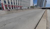 an empty road between two high rise buildings with the top of a freeway crossing to its side