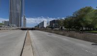 an empty road between two high rise buildings with the top of a freeway crossing to its side