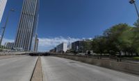 an empty road between two high rise buildings with the top of a freeway crossing to its side