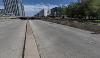 an empty road between two high rise buildings with the top of a freeway crossing to its side