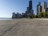 the empty road is beside water and tall buildings in the background with people walking around it