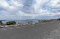 the empty road is on a hill overlooking the sea and mountains in the distance are two large, grassy hillsides